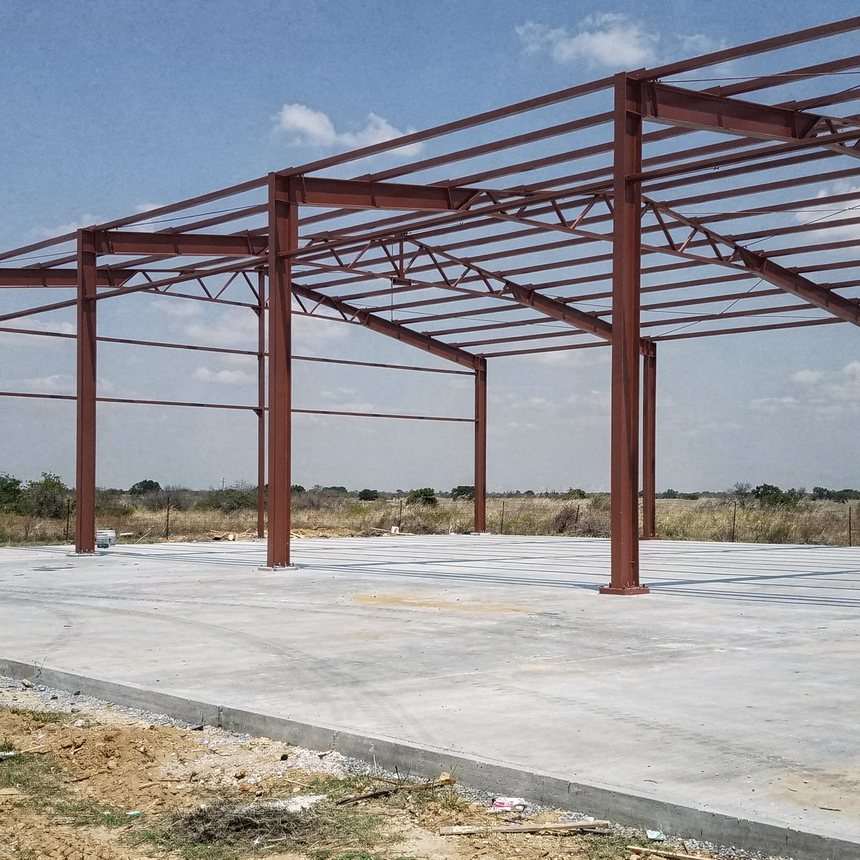Metal building under construction, slab and red-iron frame, near San Antonio, TX